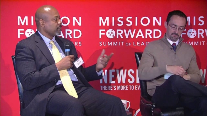 Two men on a stage with a red backdrop