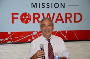 Mauricio Lim Miller smiling and holding microphone in front of a Mission Forward Sign
