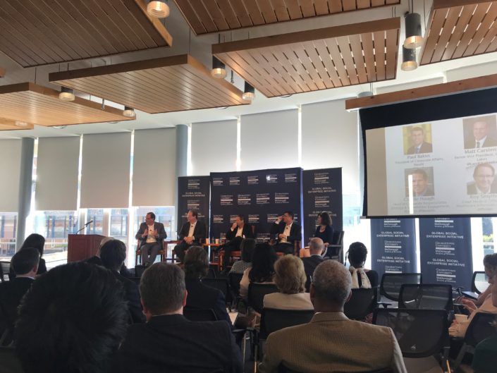 An audience in front of a stage with a panel of 5 people