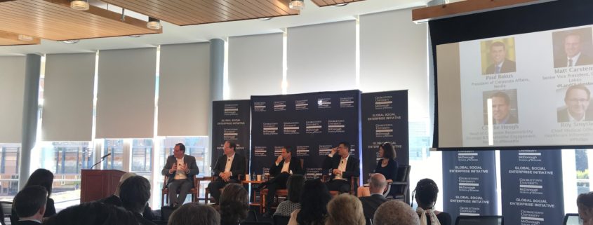 An audience in front of a stage with a panel of 5 people