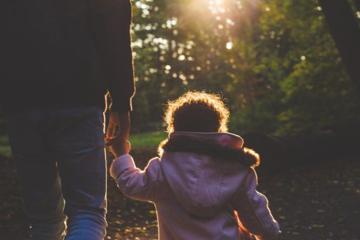 a young child in a pink winter coat holding their caregiver's hand