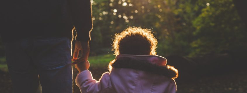 a young child in a pink winter coat holding their caregiver's hand