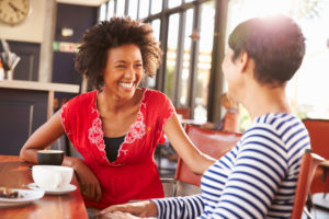 Two women smiling and talking over a coffee