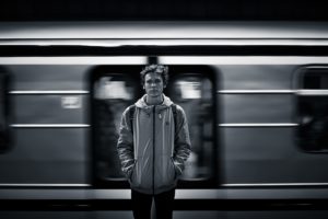 a young man looking directly at the camera as a subway train speeds behind him