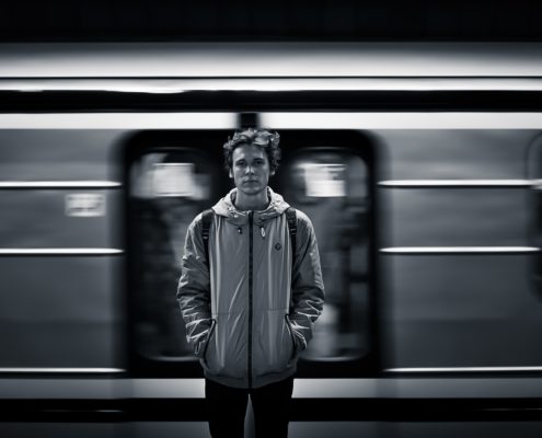 a young man looking directly at the camera as a subway train speeds behind him