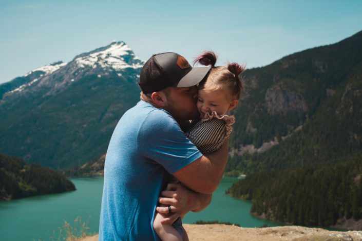 adult holding a child and giving them a hug in front of a picturesque mountain landscape
