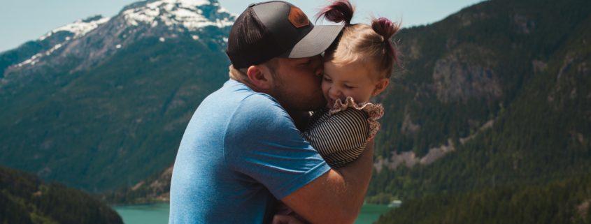 adult holding a child and giving them a hug in front of a picturesque mountain landscape