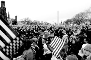 A crowd of people on the Mall in Washington, DC waving American flags. The Washington Monument is in the background.