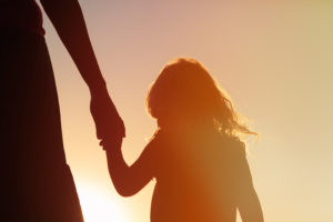 silhouette of adult holding young child's hand