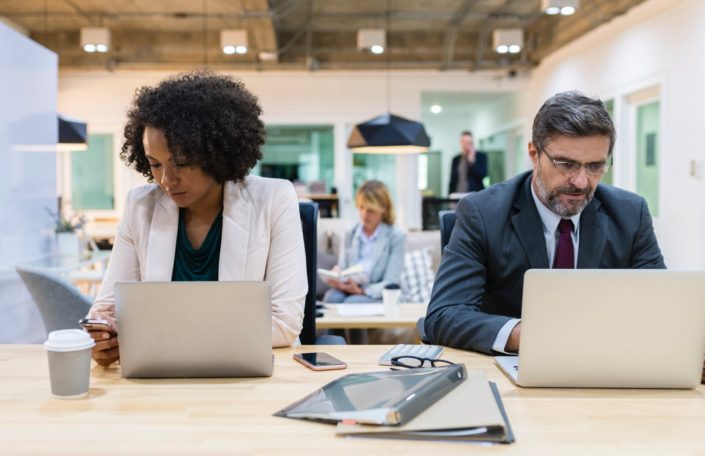 Two people of different races and genders sitting in front of their laptops
