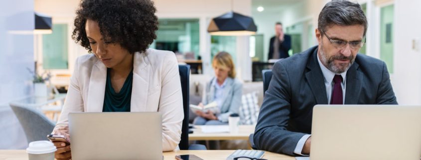 Two people of different races and genders sitting in front of their laptops