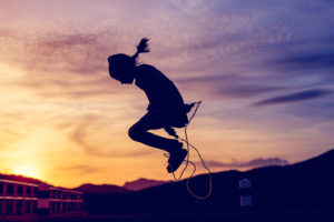 Girl jumping rope silhouetted against a sunset in the background.