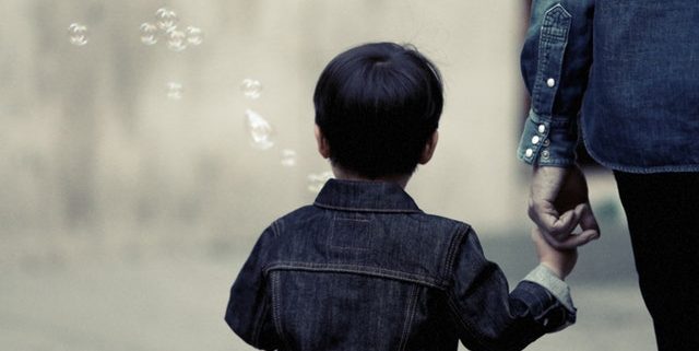 the back of a child holding an adult's hand with bubbles in the air