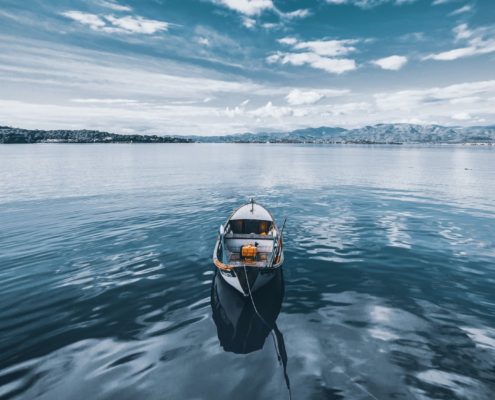 Row boat floating in the middle of water under blue skies with mountains in the background
