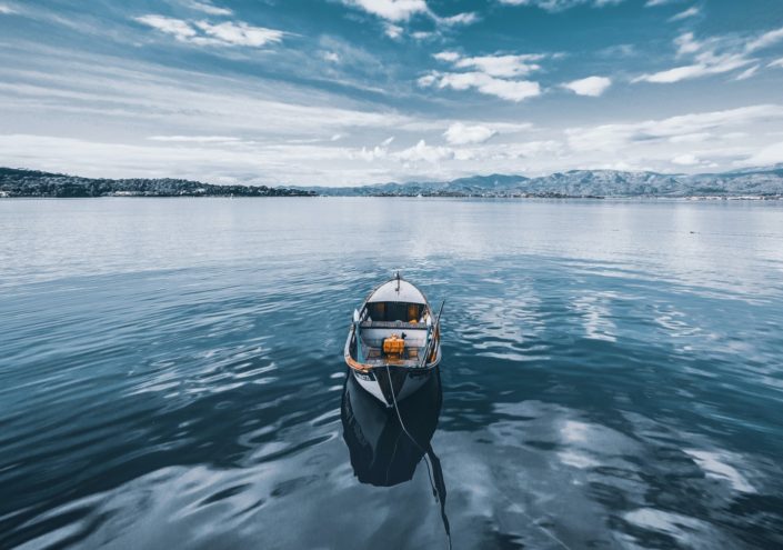 Row boat floating in the middle of water under blue skies with mountains in the background
