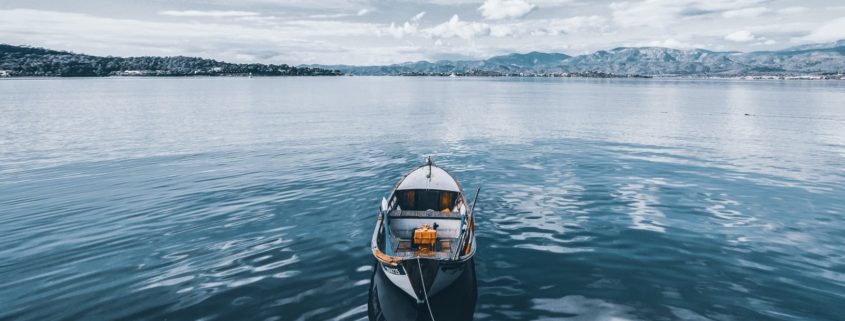 Row boat floating in the middle of water under blue skies with mountains in the background