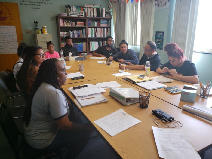 A group of students sit around a conference table, learning from Carolyn Lowery