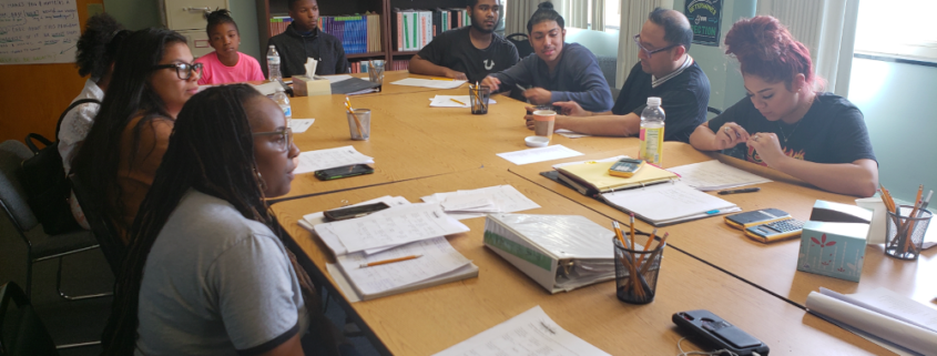 A group of students sit around a conference table, learning from Carolyn Lowery