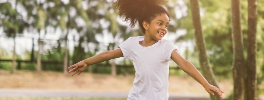 A young girl twirls around outside under the trees