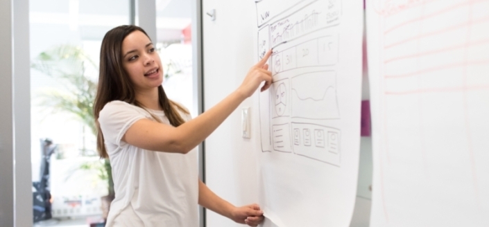 A young women leading strategy planning meeting and pointing to whiteboard diagram