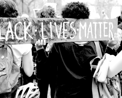 A black and white photo of protestors from behind holding a sign that says BLACK LIVES MATTER