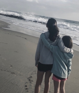 Two girls together on beach as waves crash