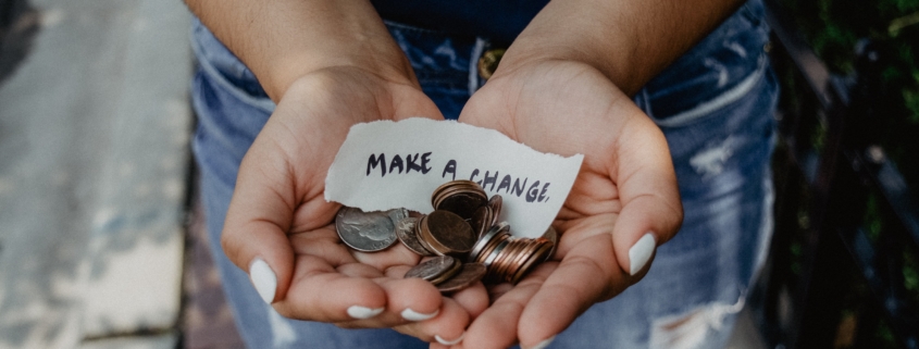 Cupped hands holding coins and paper that reads Make A Change