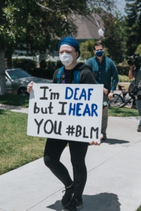 Protester with a face mask holding sign that says "I'm Deaf But I Hear You #BLM"