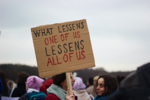 Cardboard protest sign reading What lessens one of us lessens all of us