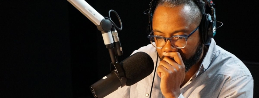 A man sits at a microphone with headphones on