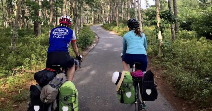 Two bikers on a paved bike trail through a green forest