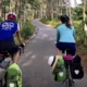 Two bikers on a paved bike trail through a green forest