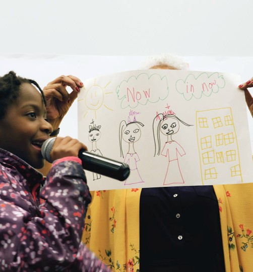 Female with a microphone holding up a drawing