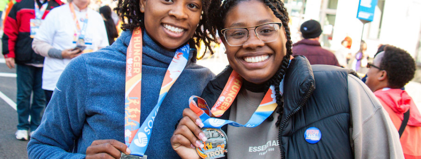 Two runners holding up the medals from the SOME Trot for Hunger around their neck