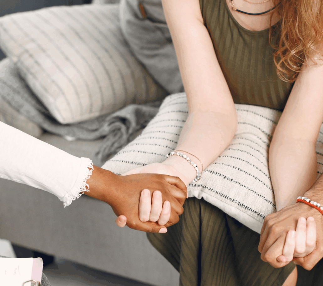 Three people sitting on chairs in a circle holding hands for comfort and support.