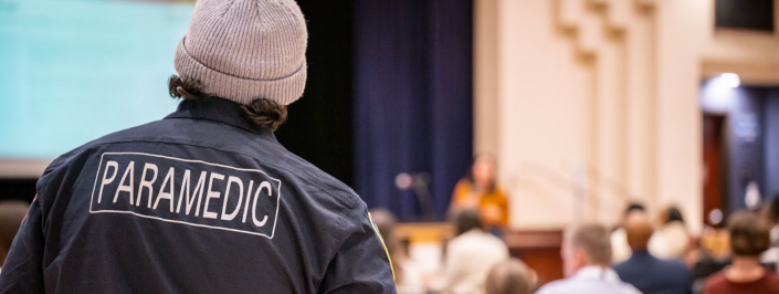 Paramedic watching and listening to a speaker at an event.
