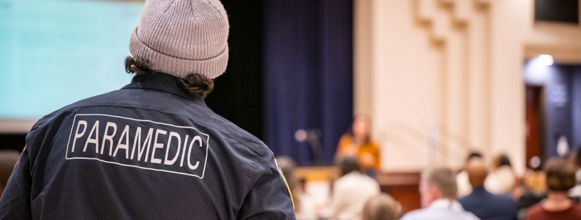 Paramedic watching and listening to a speaker at an event.